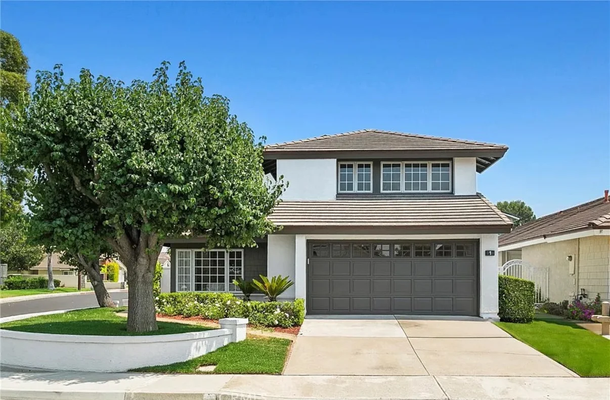 A modern two-story house with a prominent dark gray sectional garage door and concrete driveway, highlighting the choice between garage doors repair vs. replacement.