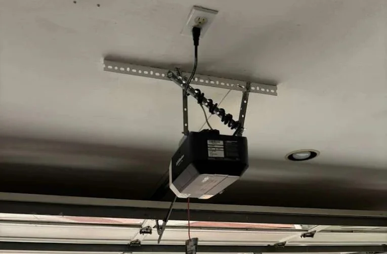 An overhead view of a black LiftMaster garage door opener motor unit mounted to the ceiling and plugged into a power outlet, illustrating common LiftMaster garage door opener issues.