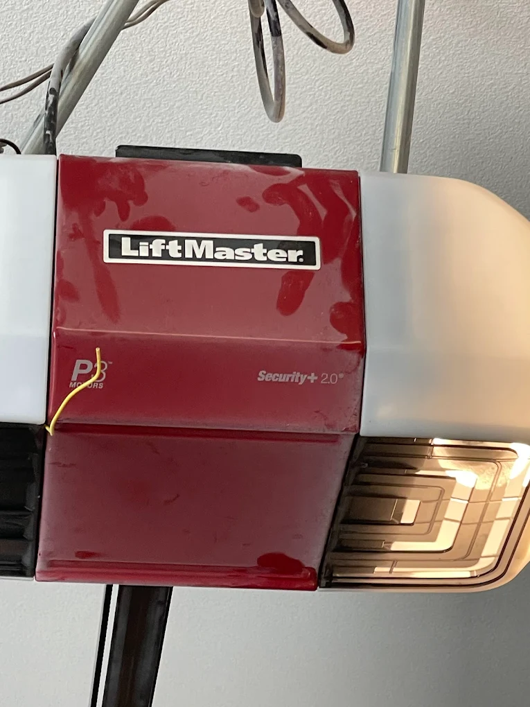 A close-up view of a red and white LiftMaster Security+ 2.0 garage door opener unit mounted to the ceiling, showing where to perform a LiftMaster garage door opener reset.