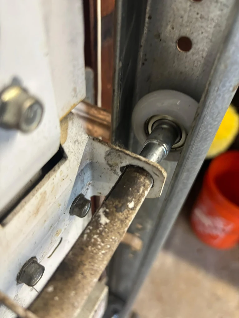 A close-up view of a white nylon garage door roller sitting inside a metal track, illustrating one of the primary hardware components to inspect when identifying common garage door squeaking causes.
