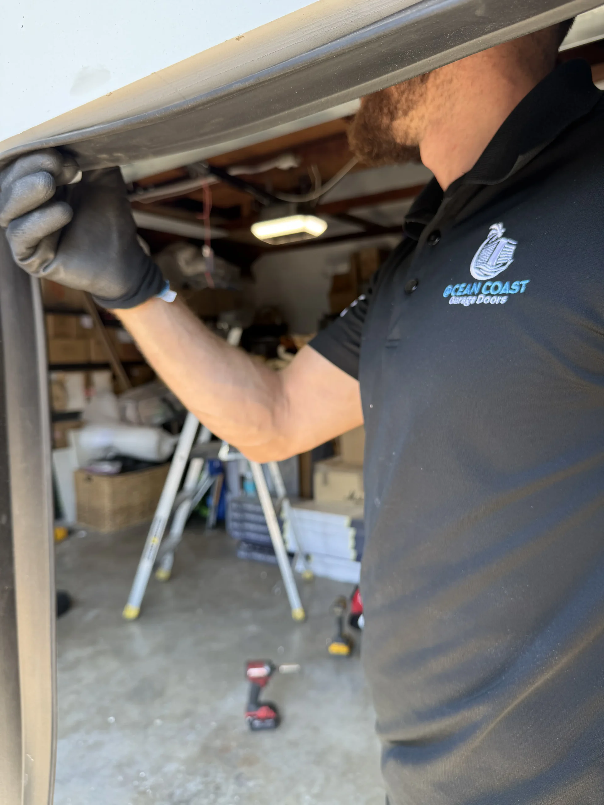 A professional technician in a black uniform inspecting a rubber weather stripping seal on a garage door frame, illustrating a routine check during regular garage door maintenance.